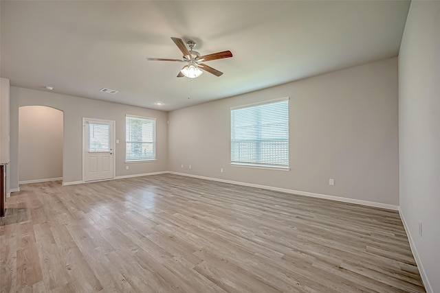 spare room featuring arched walkways, visible vents, light wood-style flooring, and baseboards