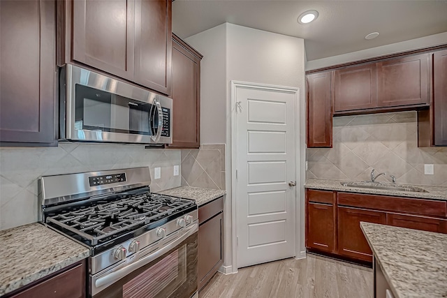 kitchen featuring light wood-style flooring, a sink, light stone countertops, stainless steel appliances, and backsplash