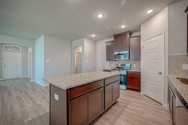 kitchen with arched walkways, light wood-style flooring, stainless steel appliances, visible vents, and a center island