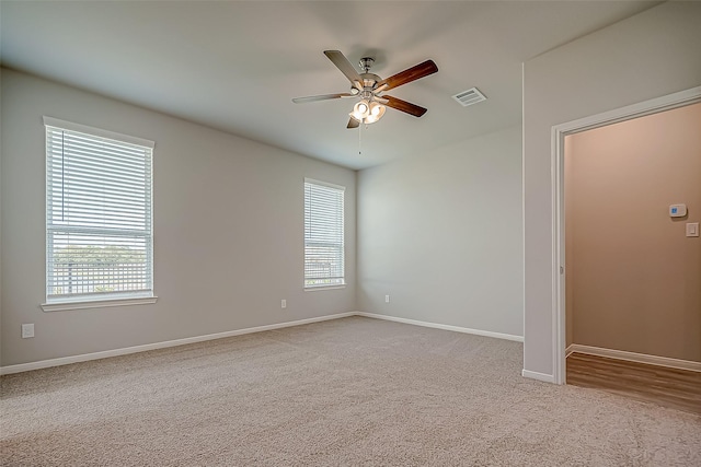 empty room with a ceiling fan, a healthy amount of sunlight, visible vents, and light carpet