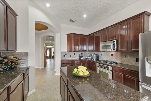 kitchen with visible vents, arched walkways, dark stone countertops, stainless steel appliances, and light tile patterned flooring