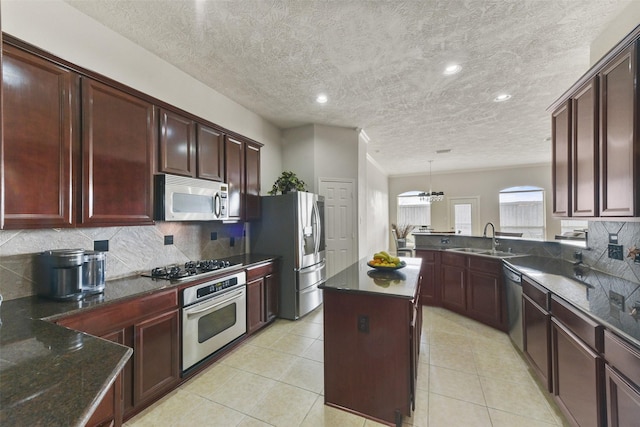 kitchen featuring a sink, hanging light fixtures, appliances with stainless steel finishes, a center island, and dark stone counters