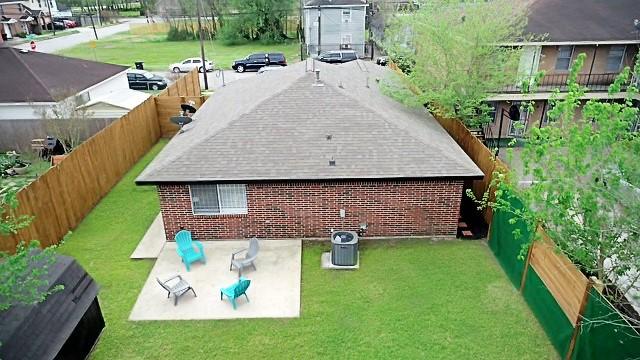 rear view of property featuring brick siding, a patio, a lawn, central AC, and a fenced backyard