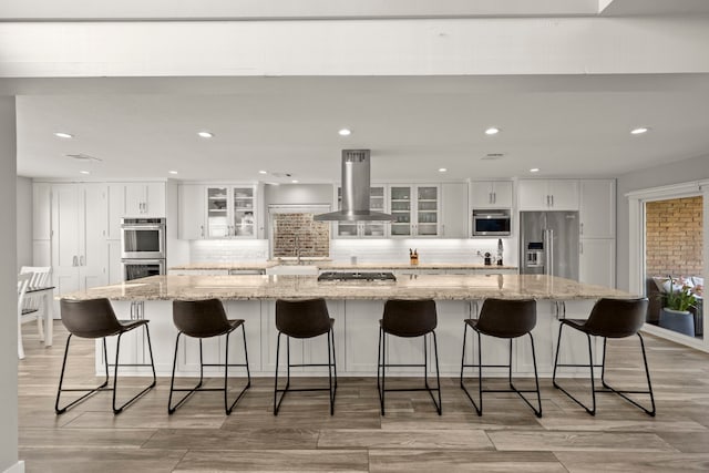 kitchen with white cabinetry, island exhaust hood, glass insert cabinets, and appliances with stainless steel finishes