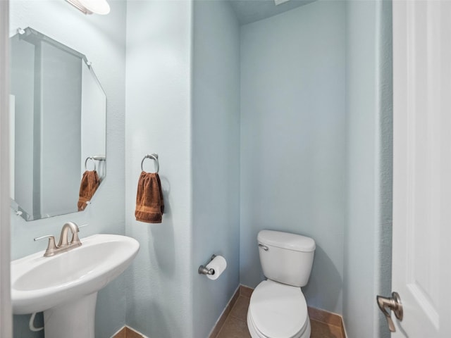 half bathroom featuring toilet, baseboards, a sink, and tile patterned floors