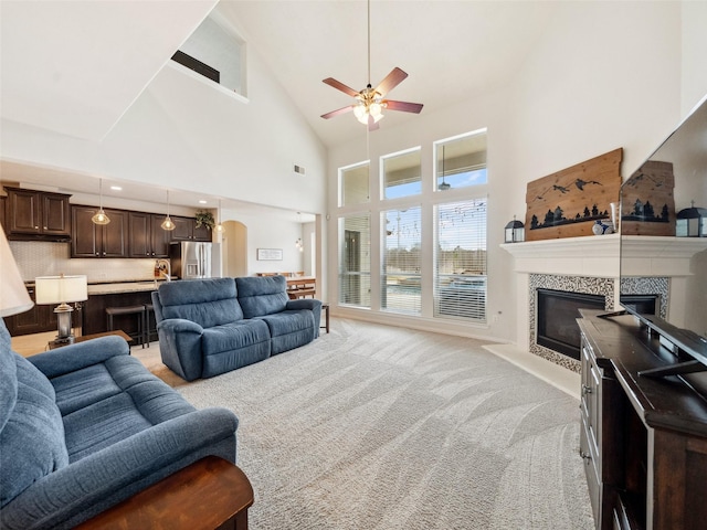 living room featuring arched walkways, a fireplace, light carpet, ceiling fan, and high vaulted ceiling