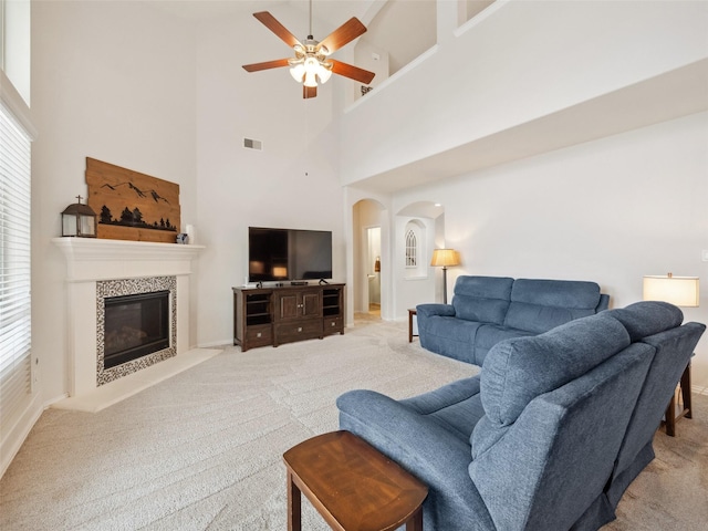 living room with arched walkways, light colored carpet, a ceiling fan, visible vents, and a tiled fireplace