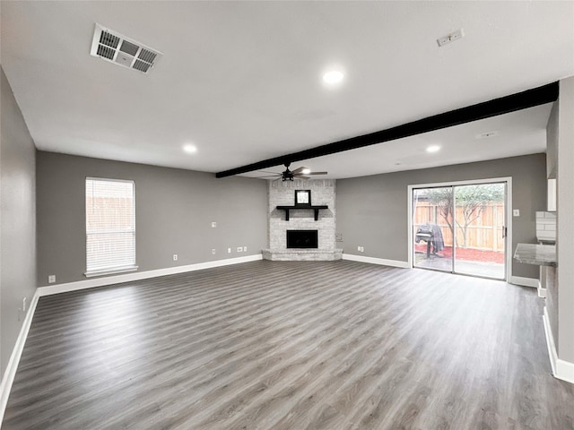 unfurnished living room featuring baseboards, visible vents, wood finished floors, a fireplace, and beam ceiling