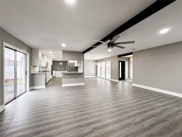 unfurnished living room featuring ceiling fan with notable chandelier, wood finished floors, and baseboards