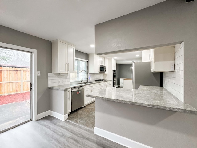 kitchen with light stone counters, stainless steel appliances, a peninsula, a sink, and white cabinetry