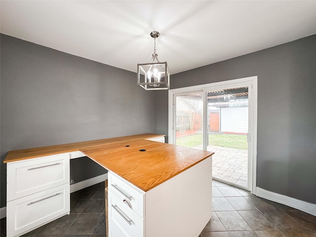 interior space featuring hanging light fixtures, an inviting chandelier, white cabinetry, butcher block countertops, and baseboards