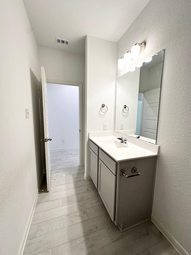 bathroom featuring a textured wall, wood finished floors, vanity, visible vents, and baseboards