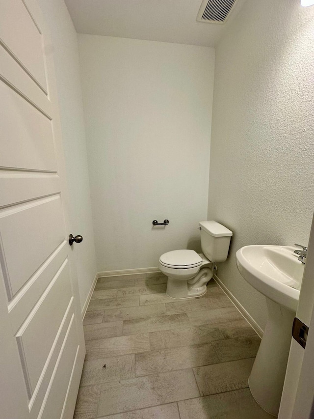 half bathroom featuring toilet, baseboards, visible vents, and wood finished floors