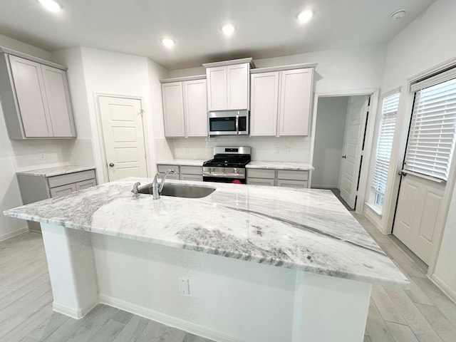 kitchen featuring appliances with stainless steel finishes, an island with sink, a sink, and light stone counters