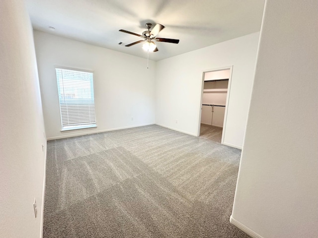 unfurnished bedroom with a ceiling fan, carpet, a walk in closet, and baseboards