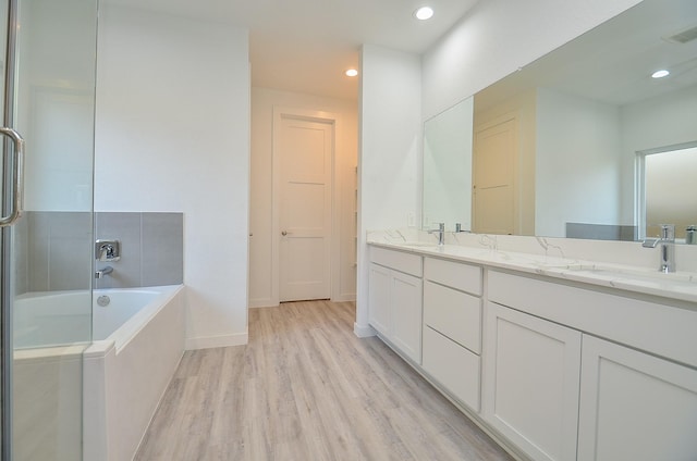 full bathroom featuring a sink, double vanity, wood finished floors, and a bathing tub