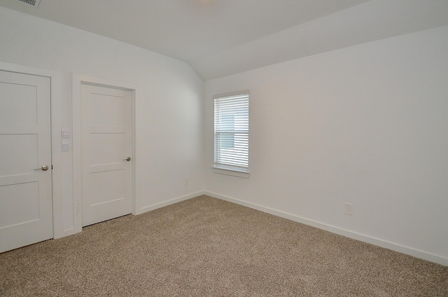 carpeted empty room featuring lofted ceiling and baseboards