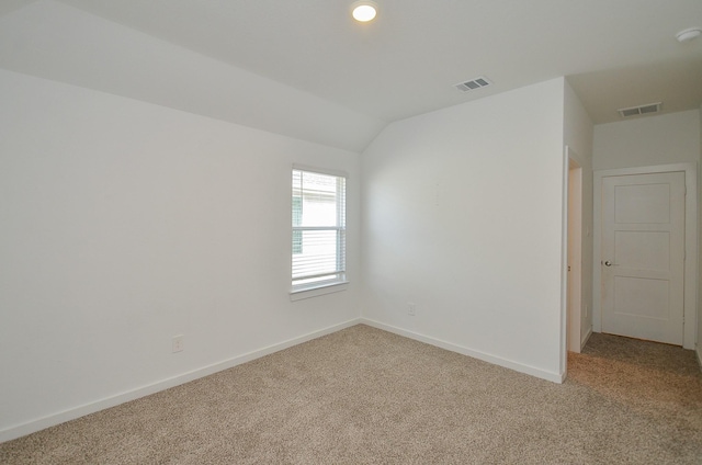 empty room with baseboards, vaulted ceiling, visible vents, and light colored carpet