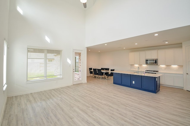 kitchen featuring a kitchen island with sink, white cabinetry, light countertops, range, and stainless steel microwave