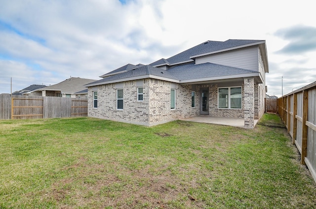 back of property with brick siding, a fenced backyard, a yard, and a patio