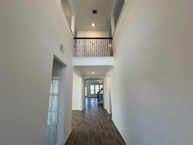 hall featuring visible vents, a towering ceiling, stairway, dark wood-type flooring, and baseboards