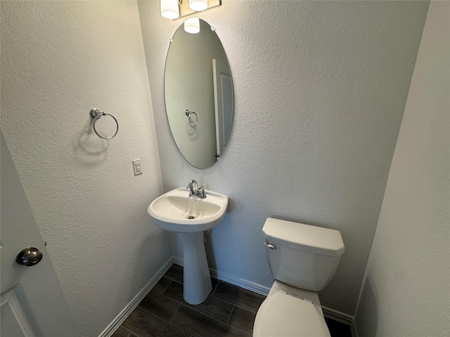 bathroom with toilet, wood tiled floor, baseboards, and a textured wall