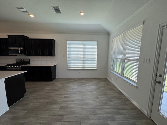 kitchen featuring dark cabinets, stainless steel appliances, vaulted ceiling, light countertops, and decorative backsplash