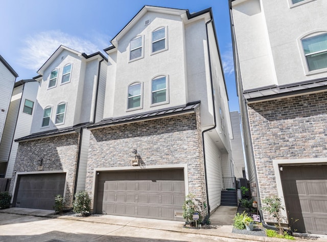 townhome / multi-family property featuring stone siding, metal roof, an attached garage, a standing seam roof, and stucco siding