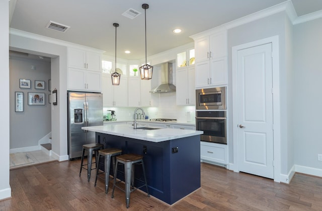 kitchen with a center island with sink, visible vents, appliances with stainless steel finishes, white cabinetry, and wall chimney range hood