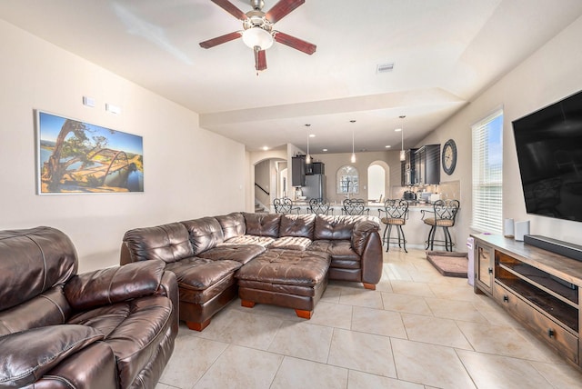 living area featuring light tile patterned floors, visible vents, arched walkways, a ceiling fan, and stairway