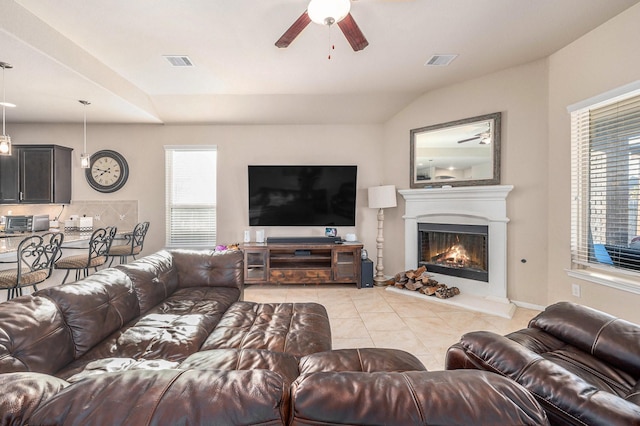 living room with light tile patterned floors, ceiling fan, a warm lit fireplace, and visible vents