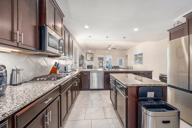 kitchen featuring light tile patterned floors, stainless steel appliances, backsplash, a kitchen island, and a peninsula