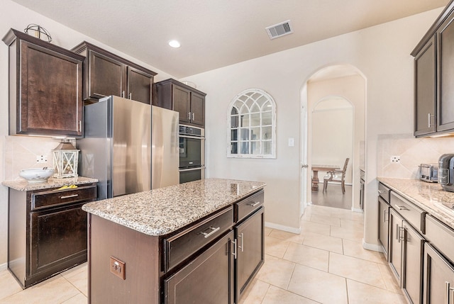 kitchen with arched walkways, visible vents, a kitchen island, stainless steel appliances, and backsplash