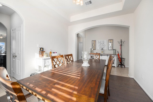 dining space with dark wood-style flooring, visible vents, arched walkways, and a tray ceiling