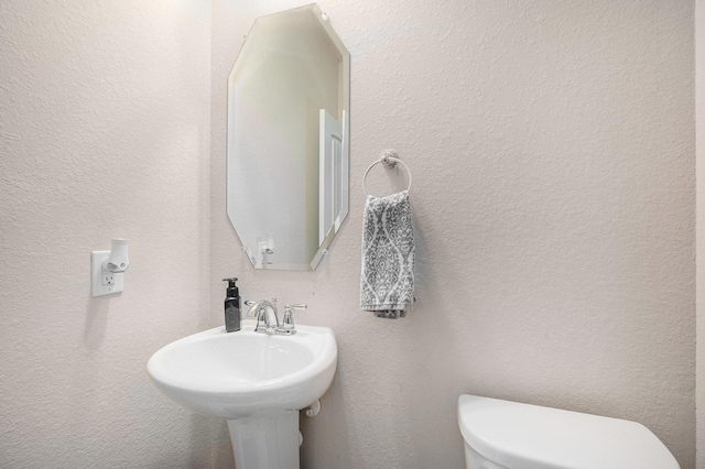 bathroom with toilet, a sink, and a textured wall