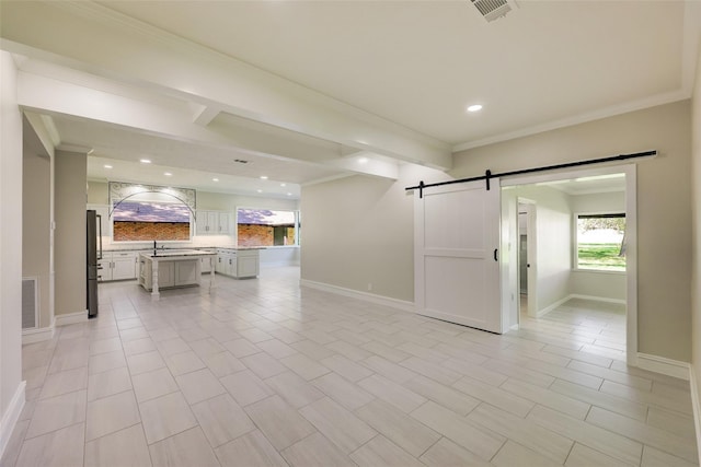 unfurnished living room with a barn door, baseboards, ornamental molding, and visible vents