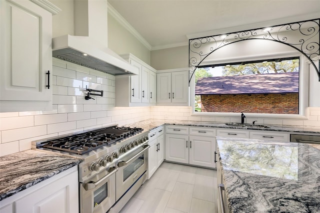 kitchen with wall chimney exhaust hood, white cabinets, a sink, double oven range, and crown molding