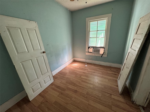 unfurnished bedroom featuring a textured ceiling, cooling unit, light wood-style flooring, and baseboards