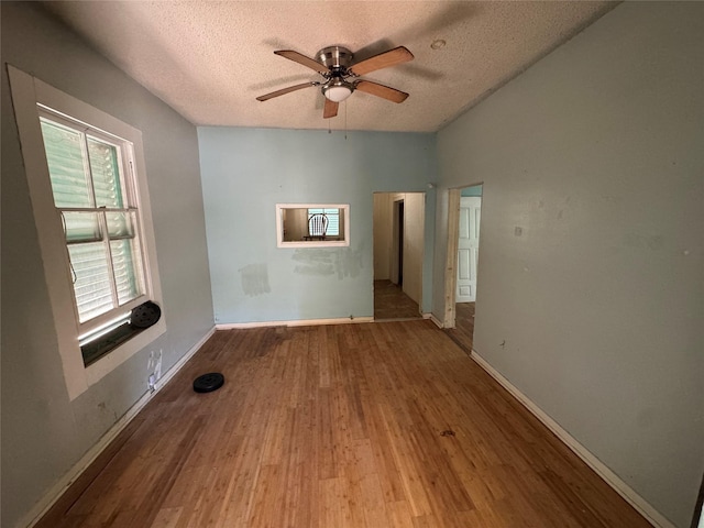 empty room featuring ceiling fan, a textured ceiling, baseboards, and wood finished floors