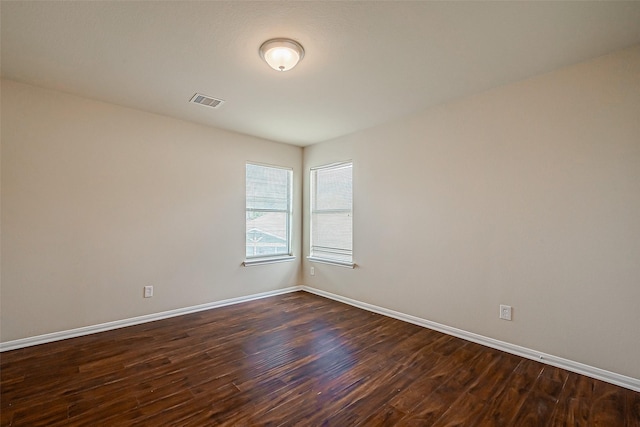 empty room featuring visible vents, dark wood finished floors, and baseboards