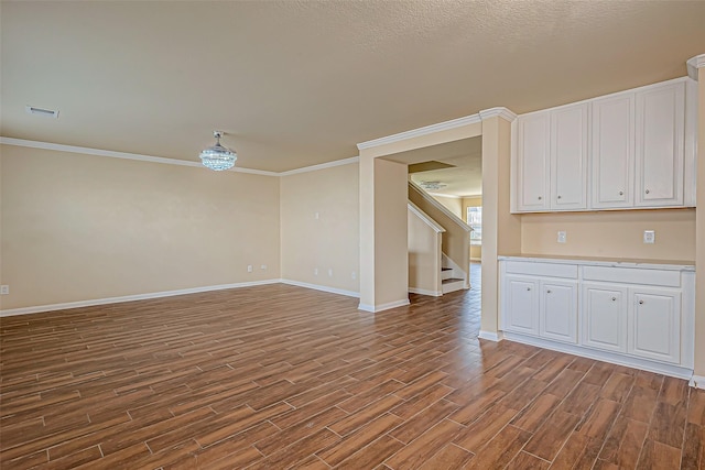 unfurnished room with wood finished floors, visible vents, baseboards, stairway, and crown molding