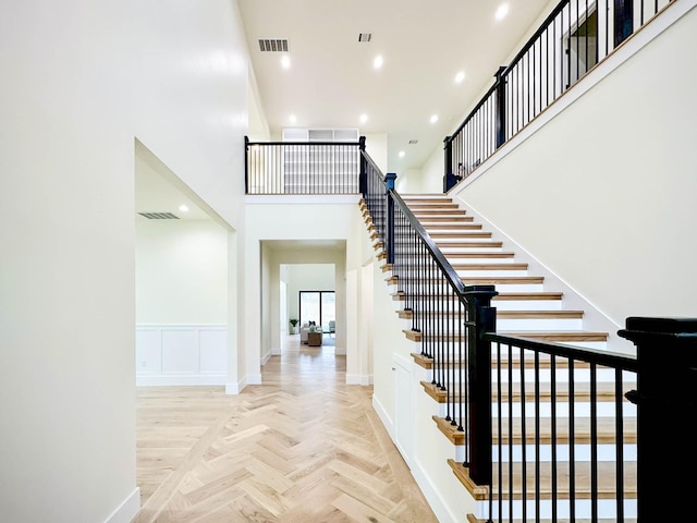 staircase with recessed lighting, visible vents, a decorative wall, and a towering ceiling