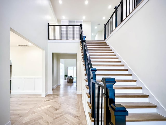 stairs with visible vents, a towering ceiling, a wainscoted wall, a decorative wall, and recessed lighting