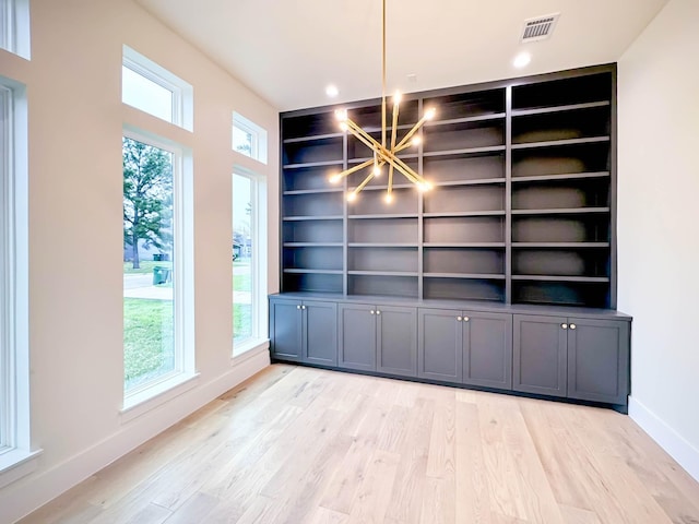 unfurnished dining area featuring a chandelier, built in shelves, visible vents, baseboards, and light wood-type flooring