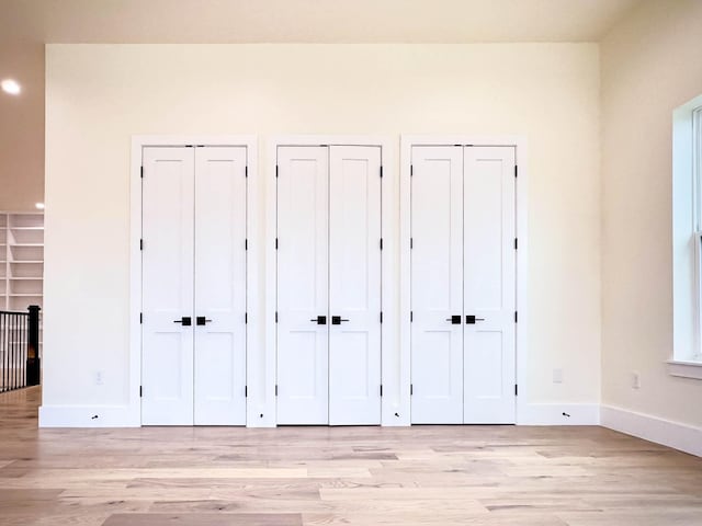 unfurnished bedroom with light wood-style floors, baseboards, and two closets