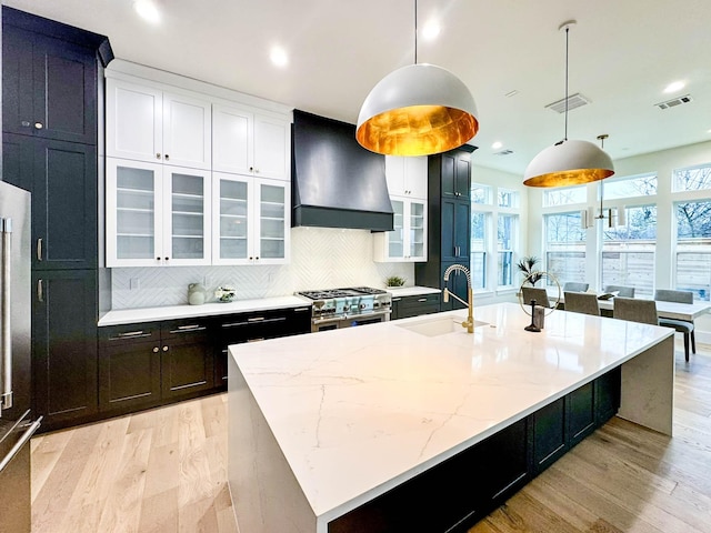 kitchen with a large island, custom range hood, glass insert cabinets, decorative light fixtures, and a sink