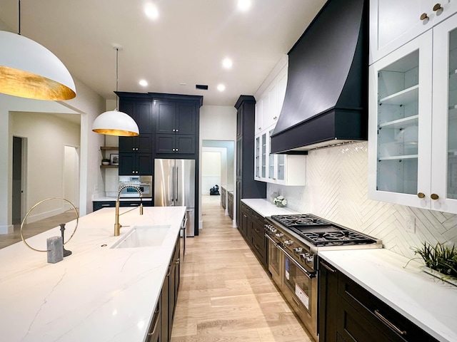 kitchen featuring glass insert cabinets, pendant lighting, premium range hood, and a sink