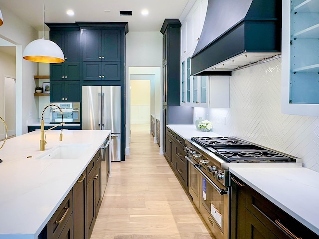 kitchen with premium appliances, custom range hood, glass insert cabinets, pendant lighting, and a sink