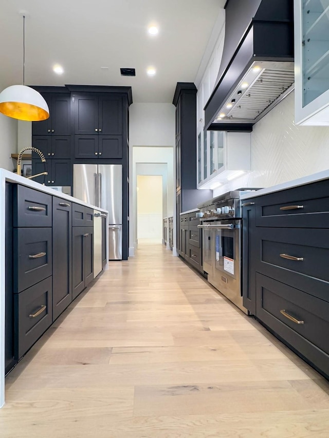 kitchen with decorative light fixtures, exhaust hood, light countertops, high end appliances, and glass insert cabinets