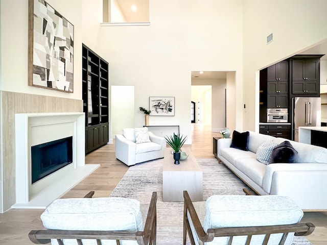 living room featuring a fireplace with raised hearth, visible vents, and light wood-style flooring